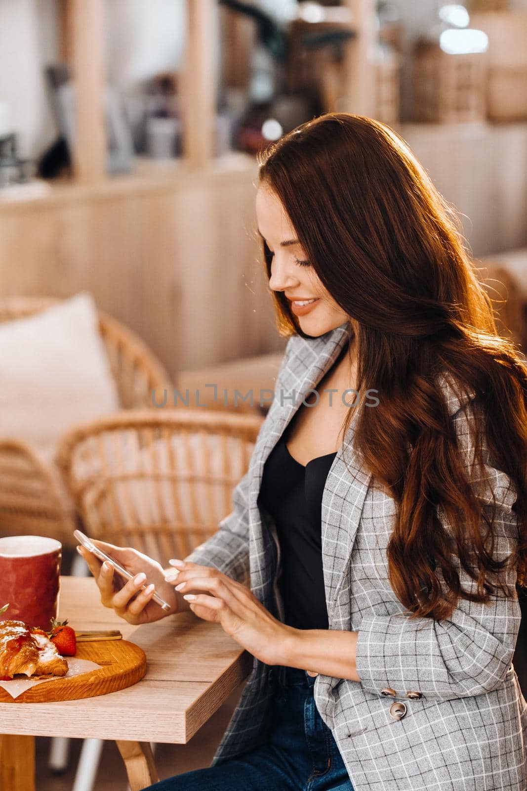 A girl is sitting at a table and texting on her smartphone in a cafe.A girl is sitting in a coffee shop with a phone.Writes in the phone.