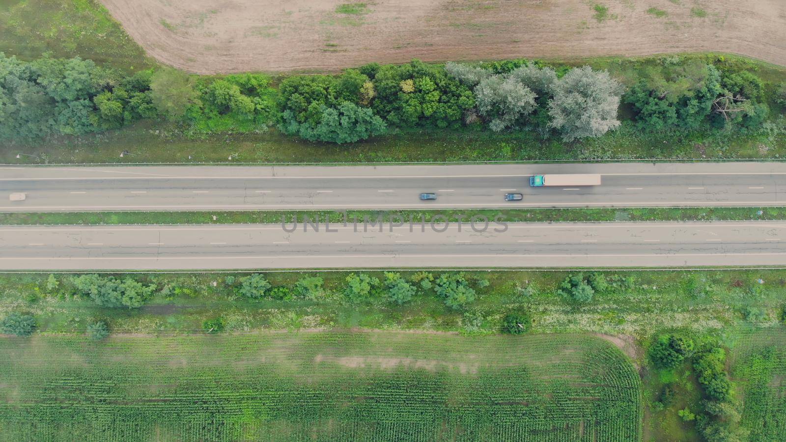 Speedway next to the forest and fields, a view from above from the clouds. On the road there are trucks and cars