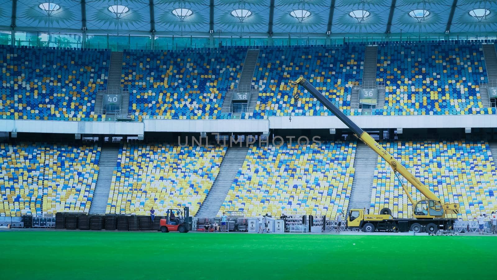 View on the football stadium with workers. colored chairs in ukrainian. crane large machine