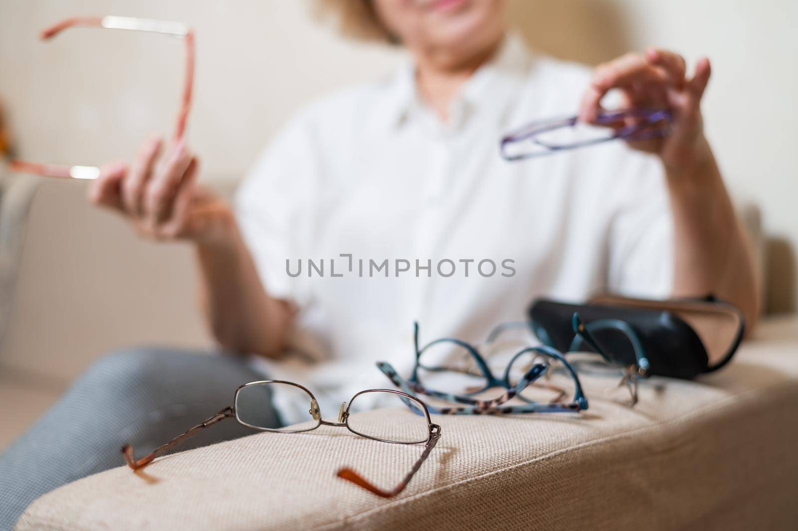 An elderly Caucasian woman chooses glasses from her home collection.