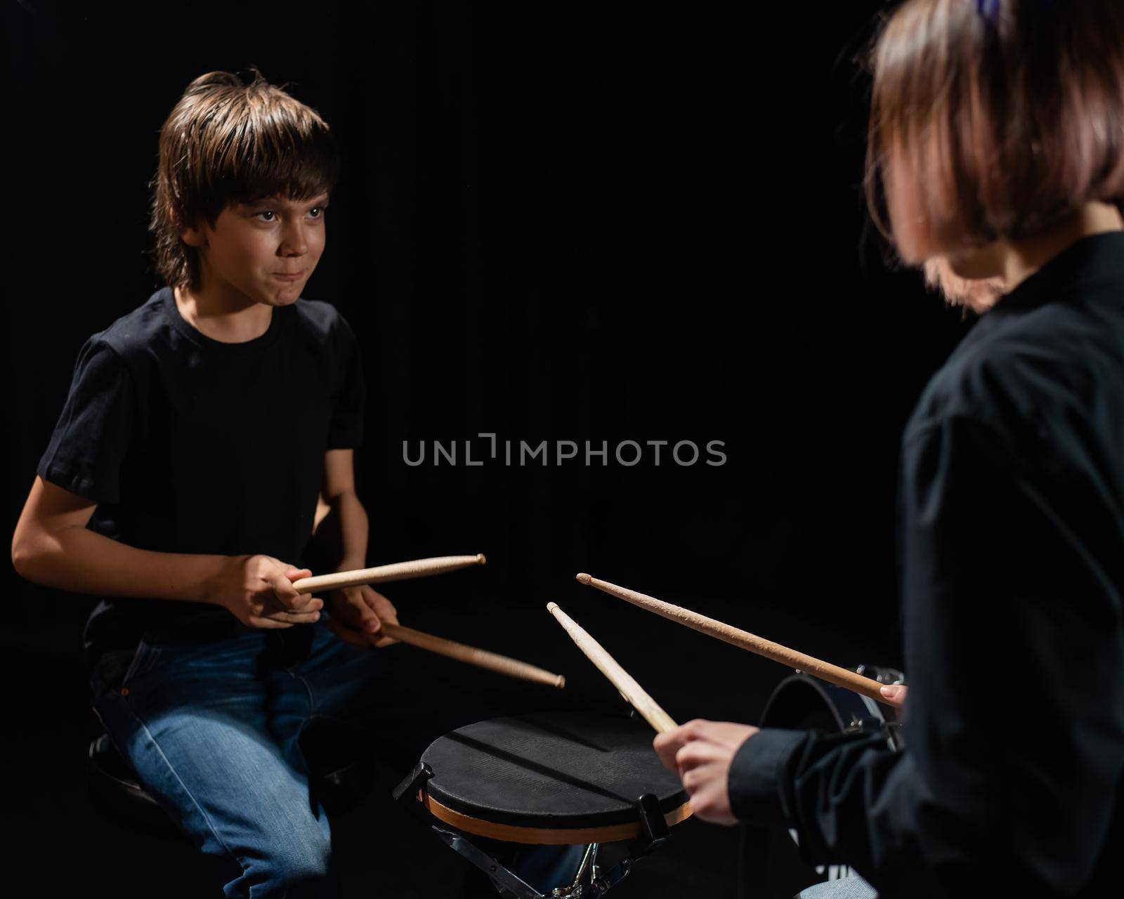 Young caucasian woman teaches a boy to play the drums in the studio on a black background. Music school student by mrwed54