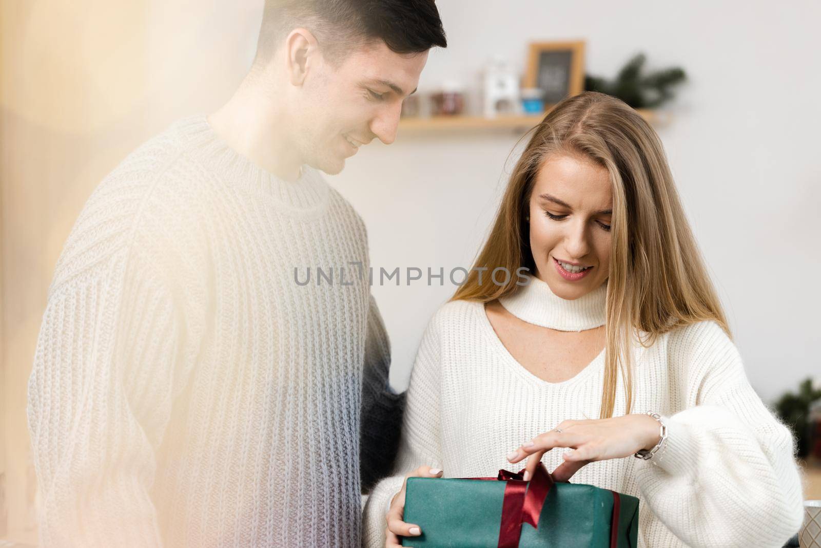 Sweet young couple opening Christmas gifts in the living room at home