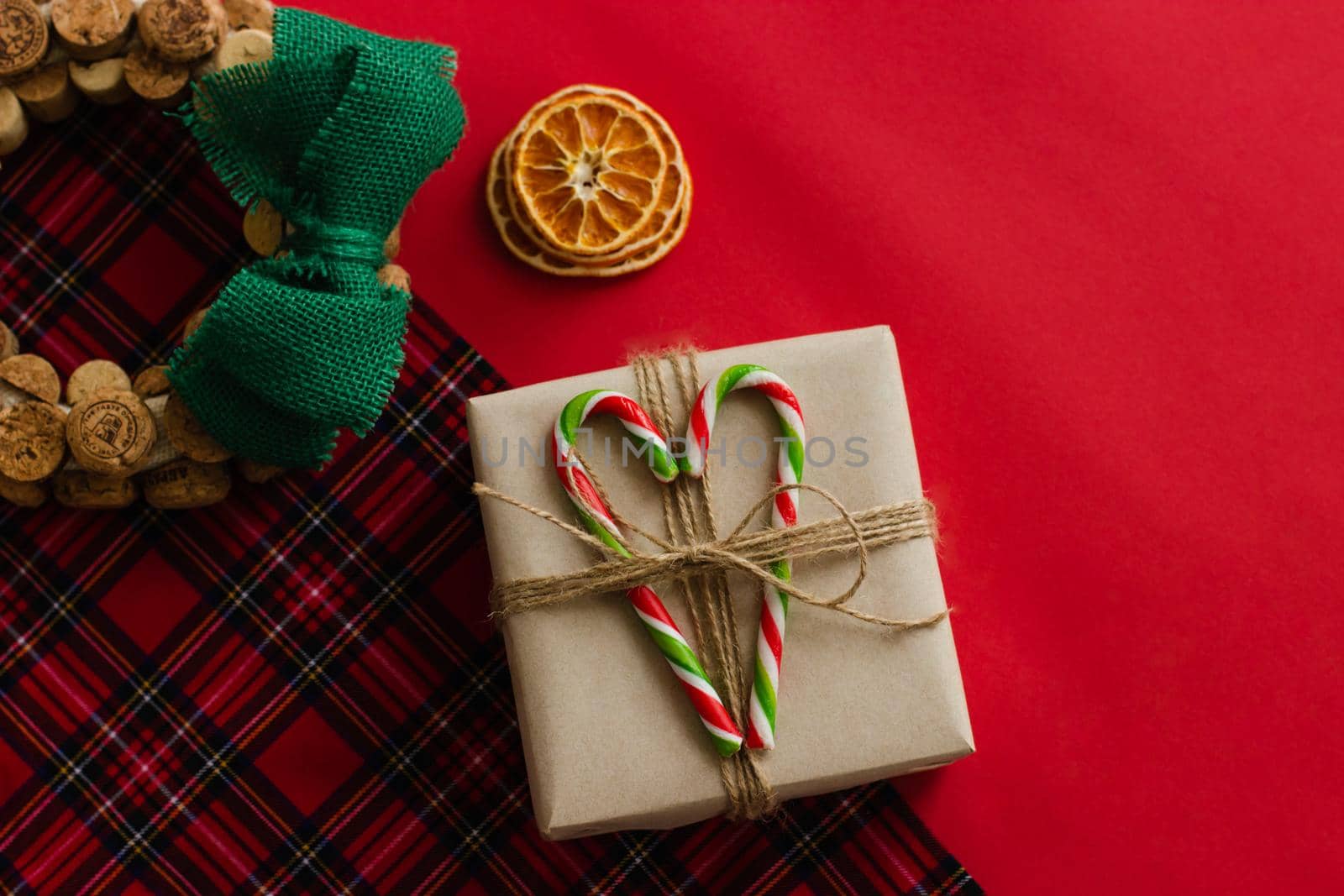 Christmas wreath and handmade gift. Checkered background. Christmas lollipops. Dried oranges. Homemade wreath of corks and linen green bow.