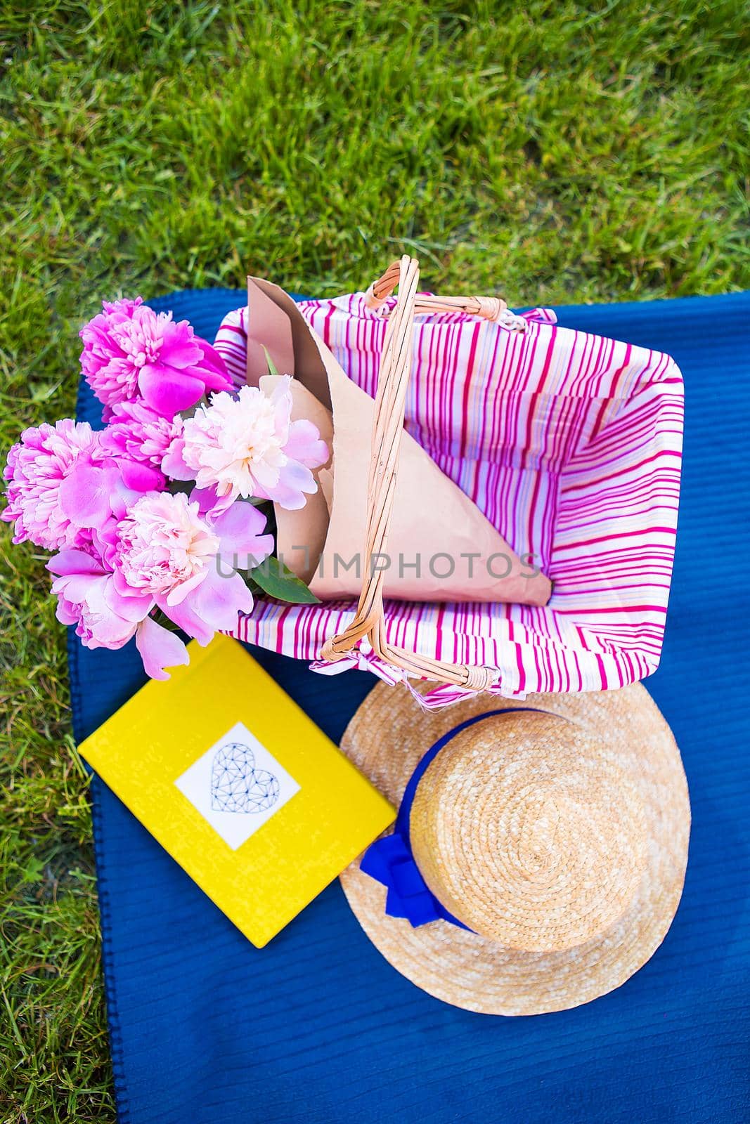 Beautiful flowers in a basket and yellow album lie on the grass-bright picnic