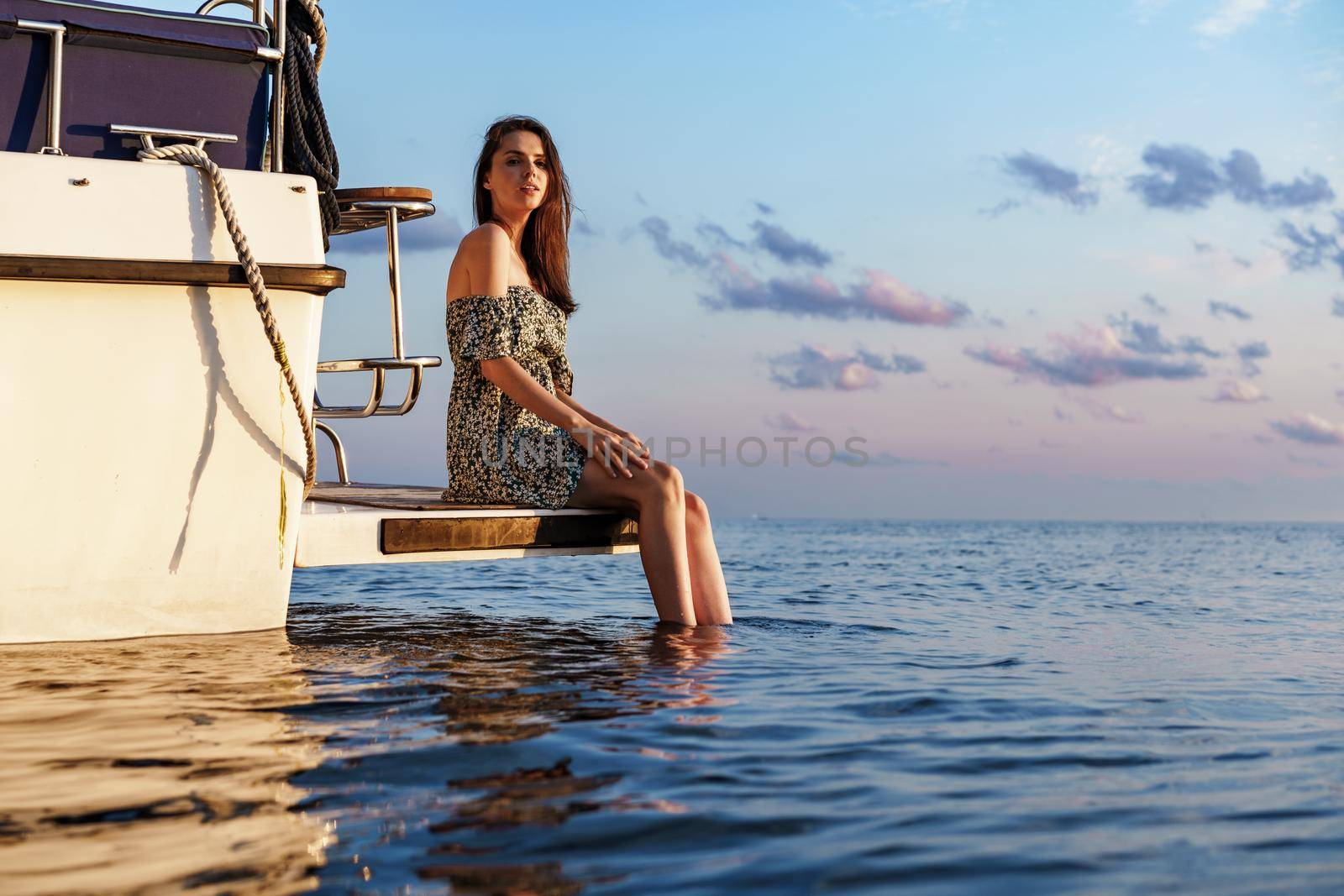 Girl sits on the edge of the yacht with legs splashing in sea water, close up