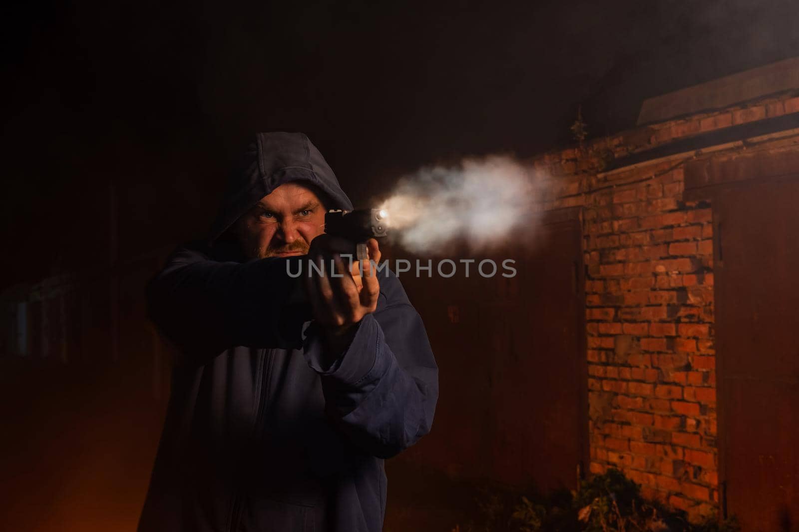 Caucasian man in a hood shoots a pistol. by mrwed54