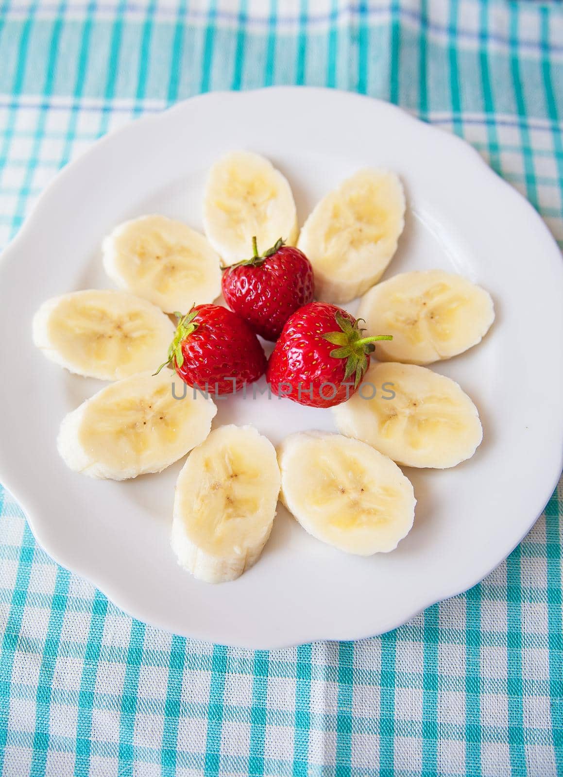 banana and strawberries on a white plate and a colorful napkin