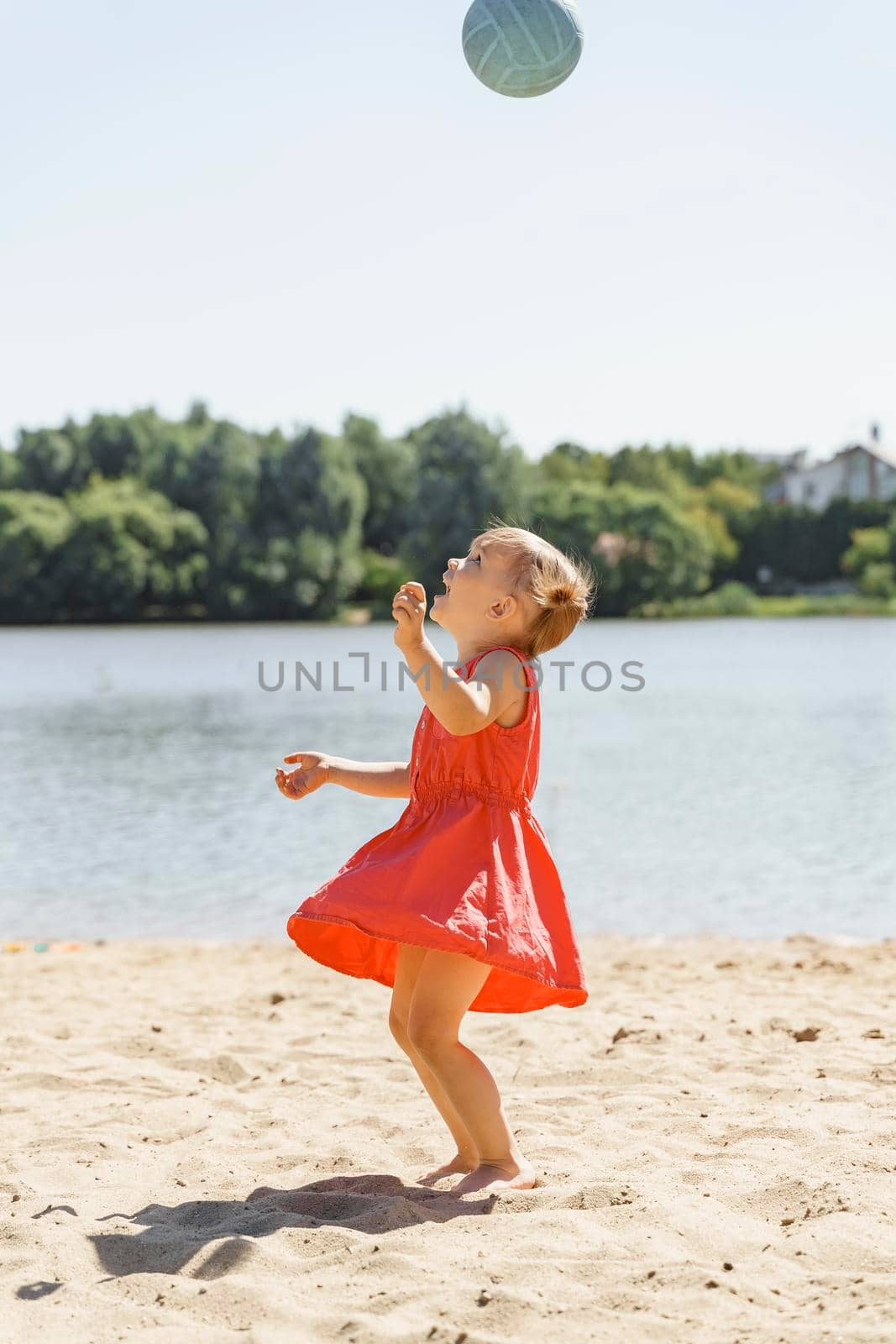 cute little girl in a red dress plays with a ball on the sand by Lena_Ogurtsova