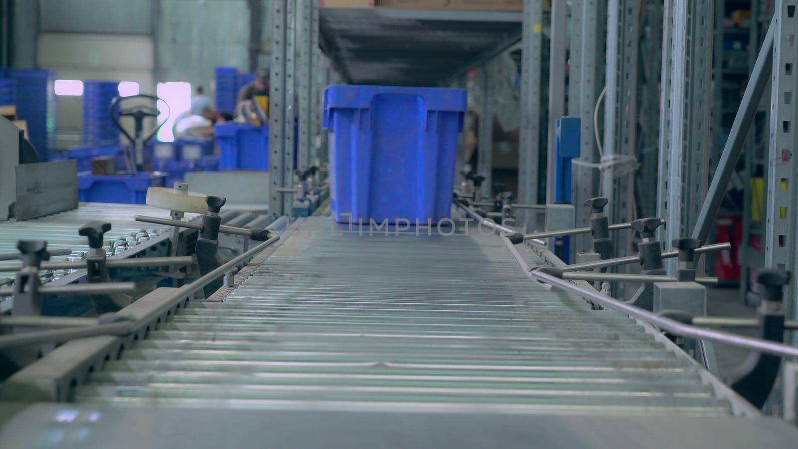 close up parcels in blue box on conveyor sorted for dispatch. On the background working workers in warehouse.