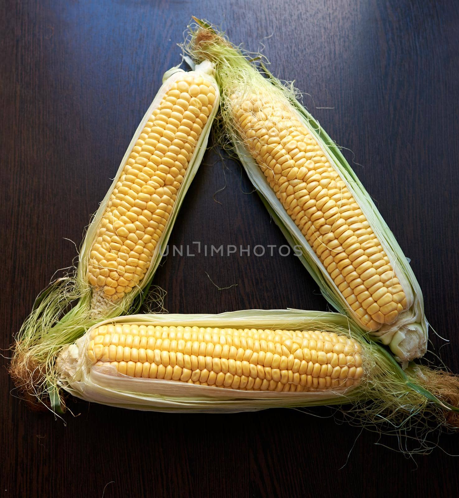 Four golden ears of corn with leaves. Low key. Top view