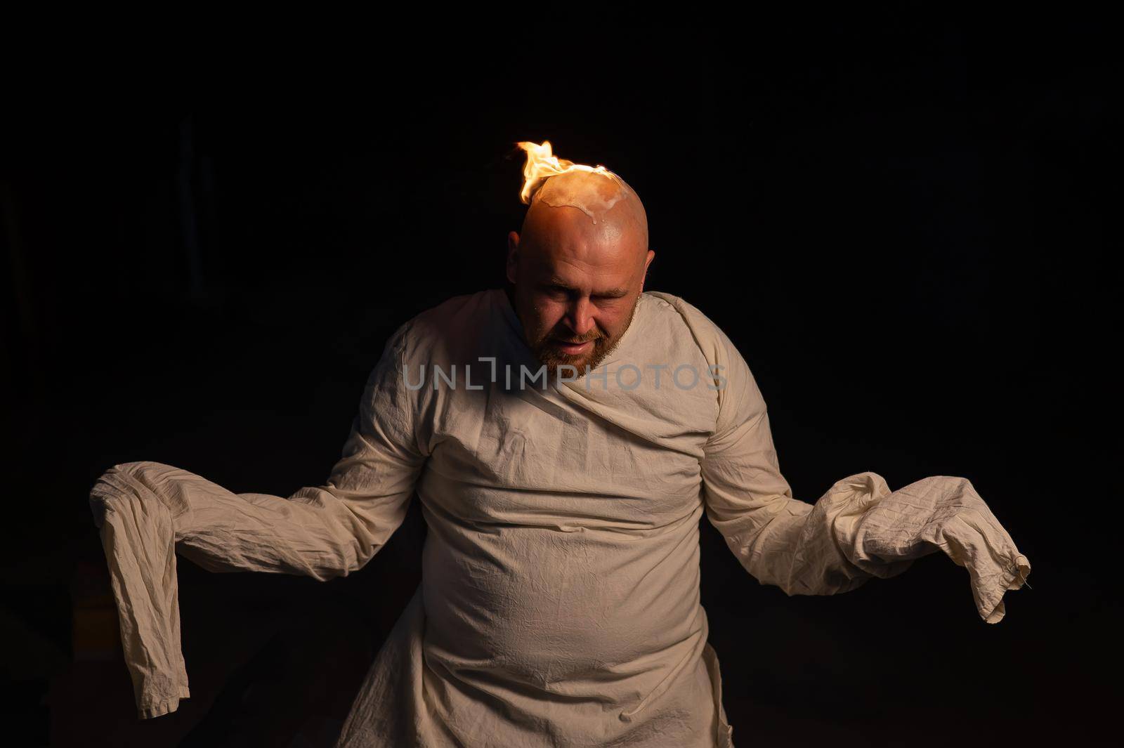Bald man in a straitjacket with a burning head on a dark background