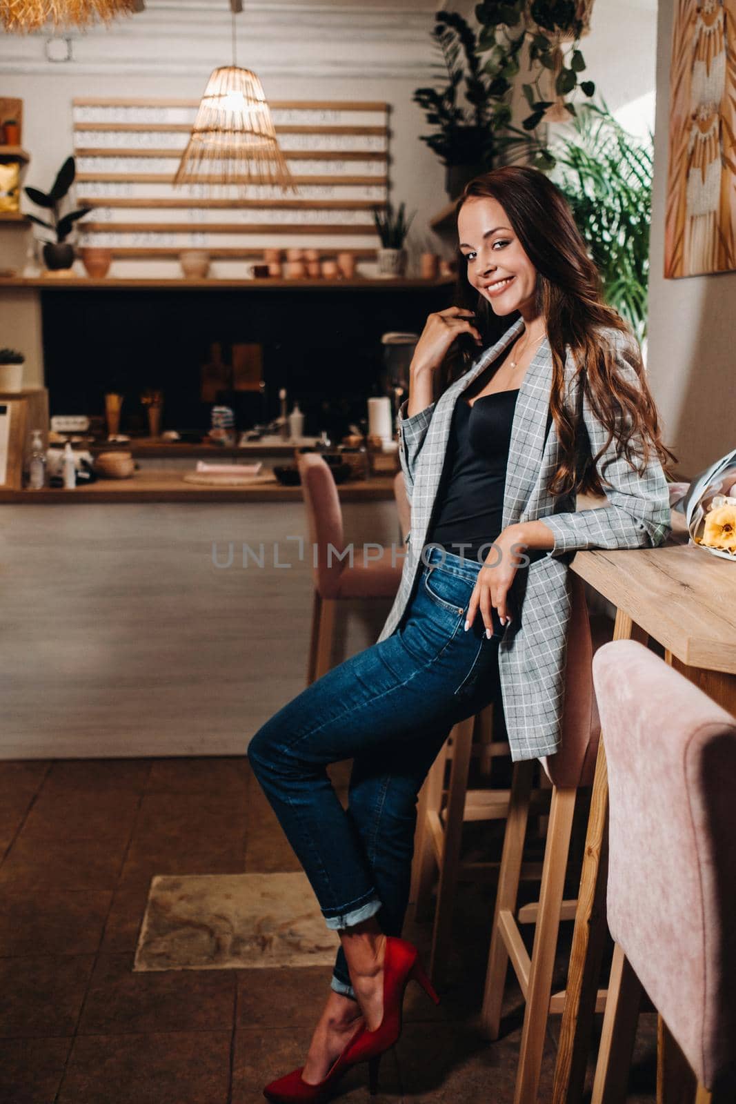 Portrait of a young European girl with long hair in a coffee shop in the evening light, a tall Girl in a jacket with long hair in a cafe by Lobachad