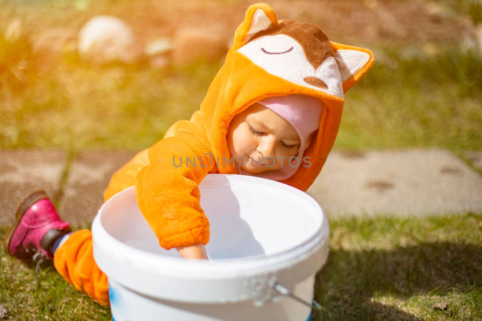 adorable little toddler playing with water in the backyard in sunshine. child in a fox costume