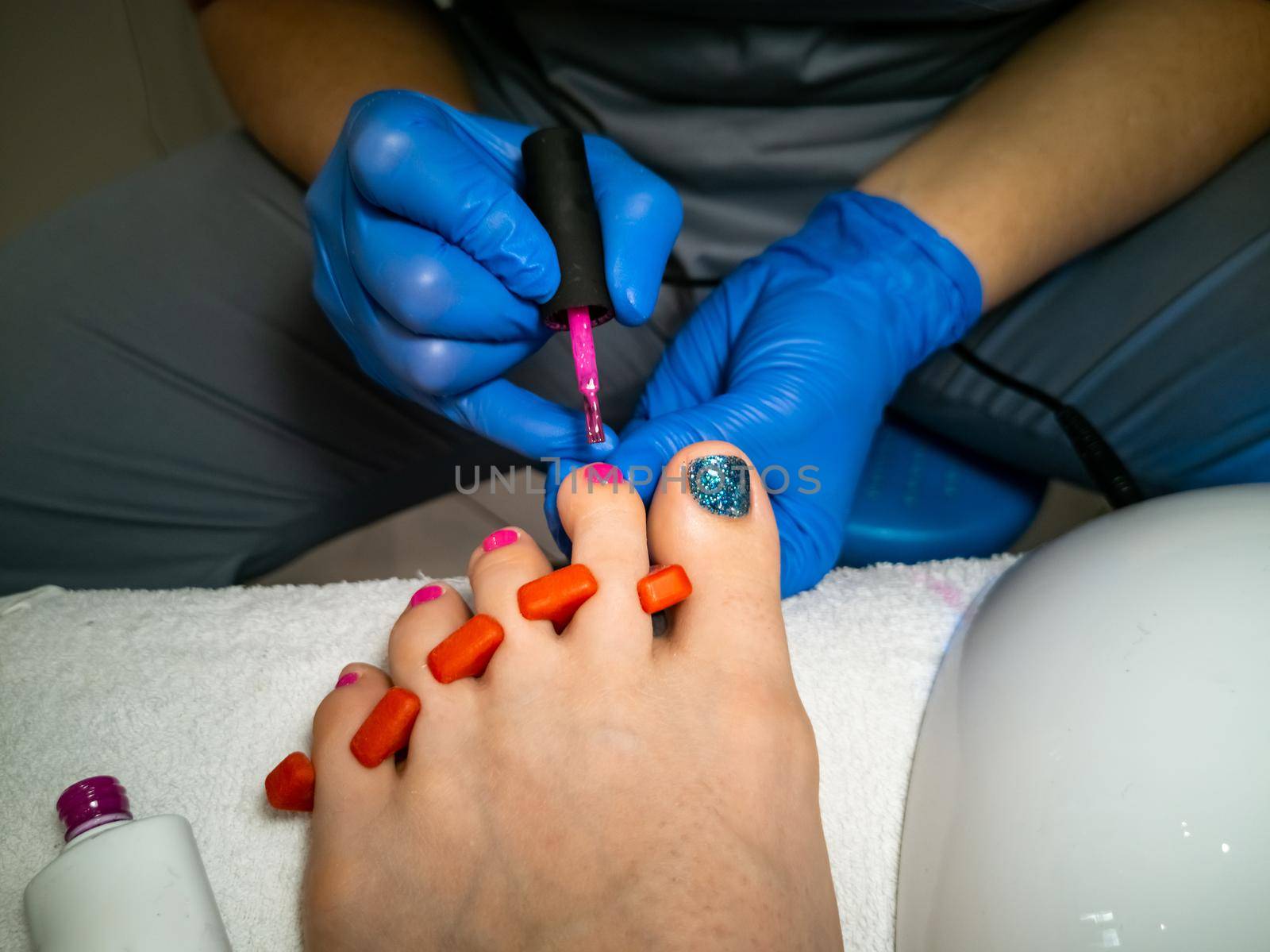 gloved master makes a pedicure for a client. close-up no face. woman in a nail salon paints her nails with varnish by Mariaprovector