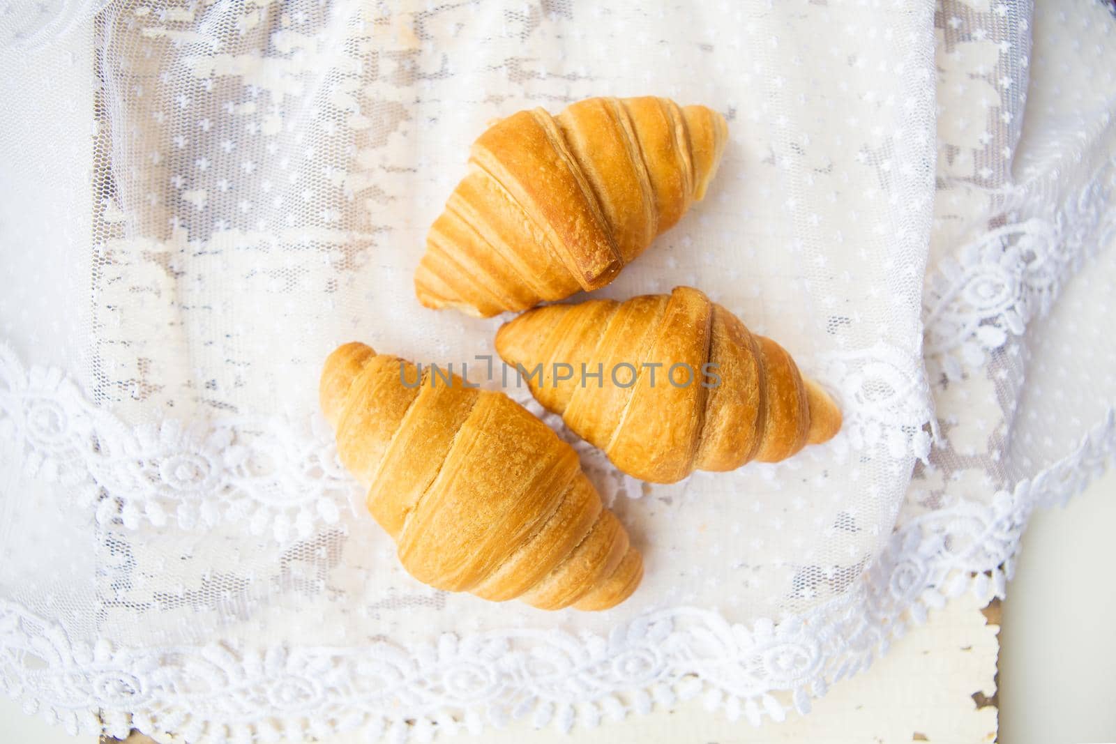 Beautiful and delicious croissants on the background of old laces and white table by sfinks