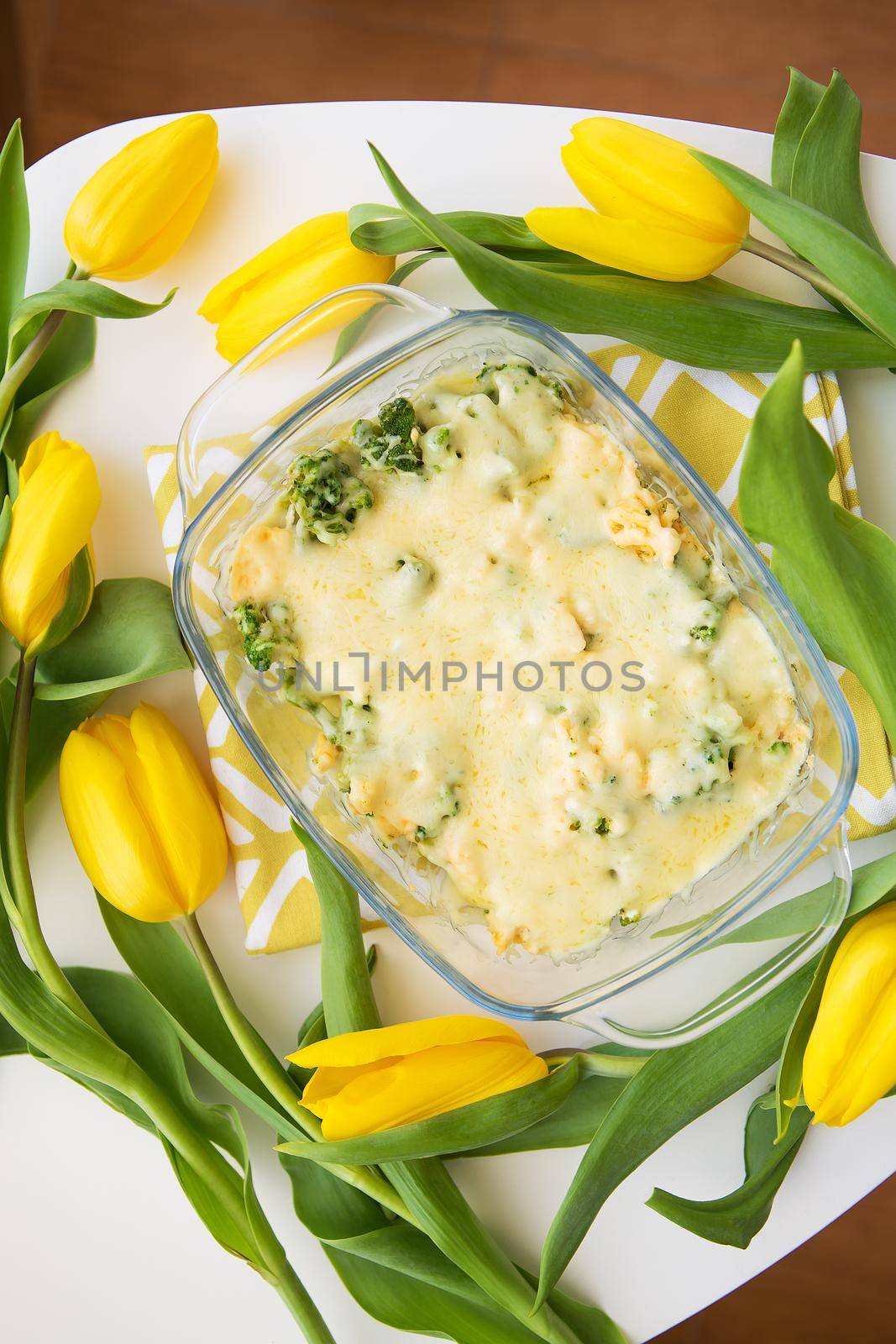 tasty casserole with broccoli, cheese and cream on a background of yellow tulips