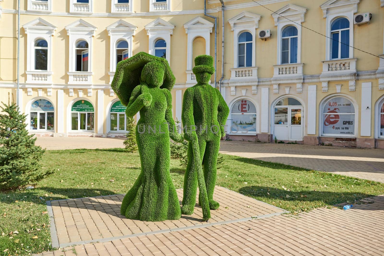 Topiary sculpture of lady with umbrella and dressed in flared skirt and jentleman with a cane and a top hat