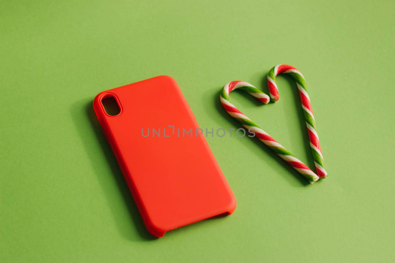 Red smartphone case on a green background. Christmas lollipops. Heart of lollipops.