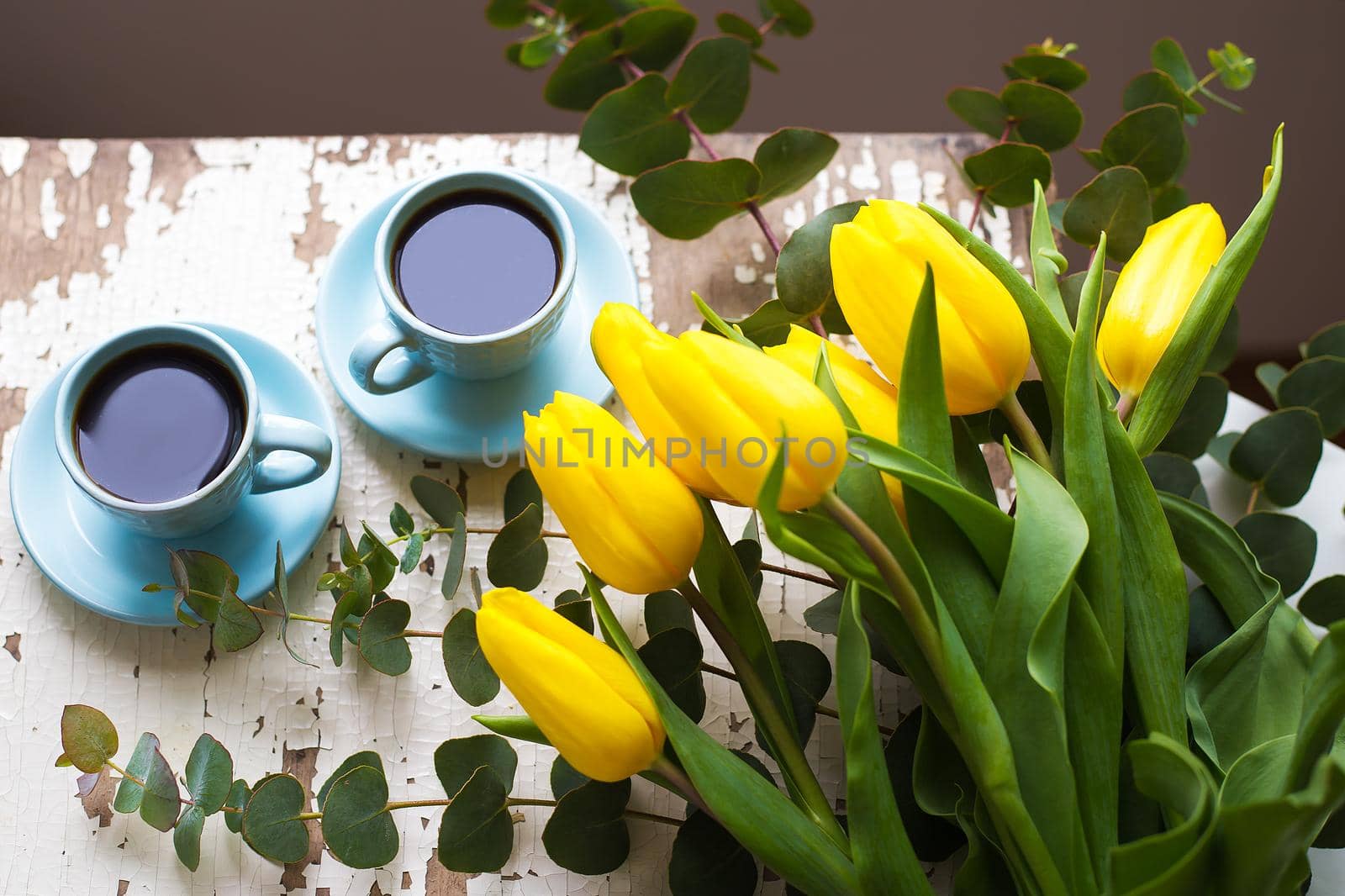 two blue cup of coffee with yellow tulips on an old table