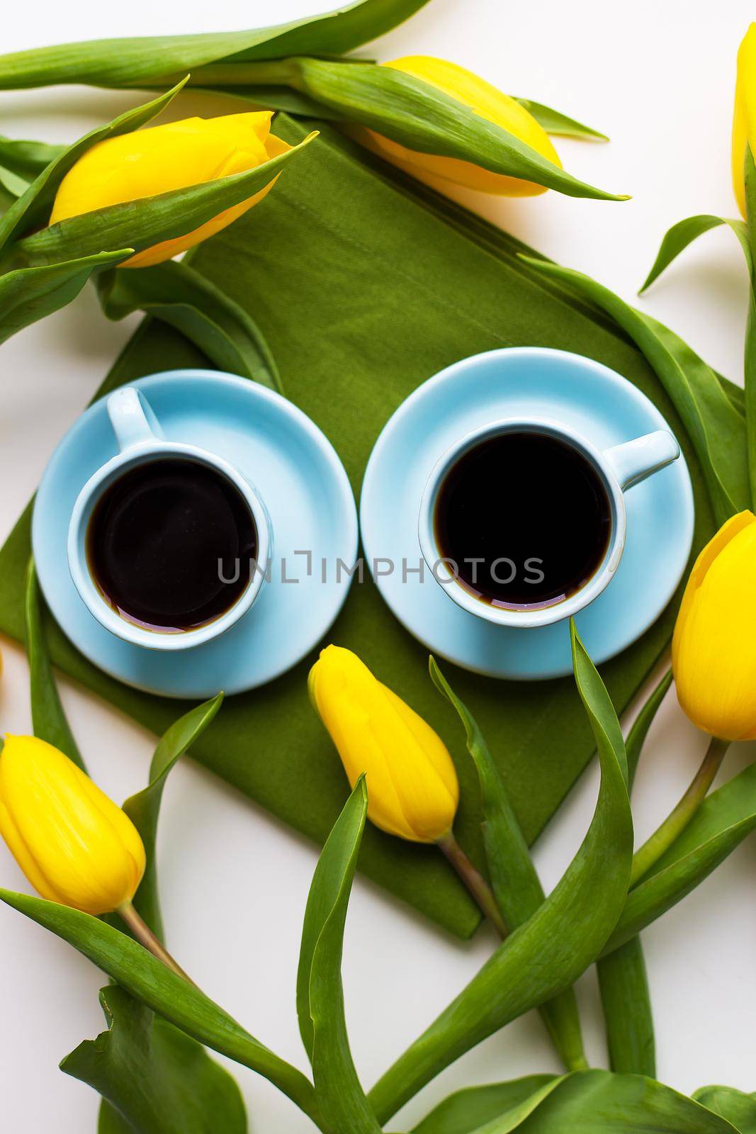 two blue cups of coffee on a table with green cloth and yellow tulips