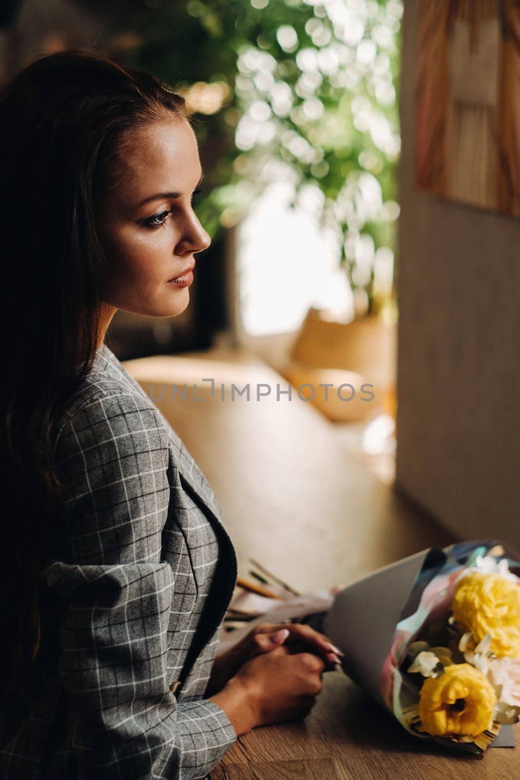Portrait of a young European girl with long hair in a cafe with a bouquet standing near the window, a tall girl in a jacket with long hair in a cafe waiting.