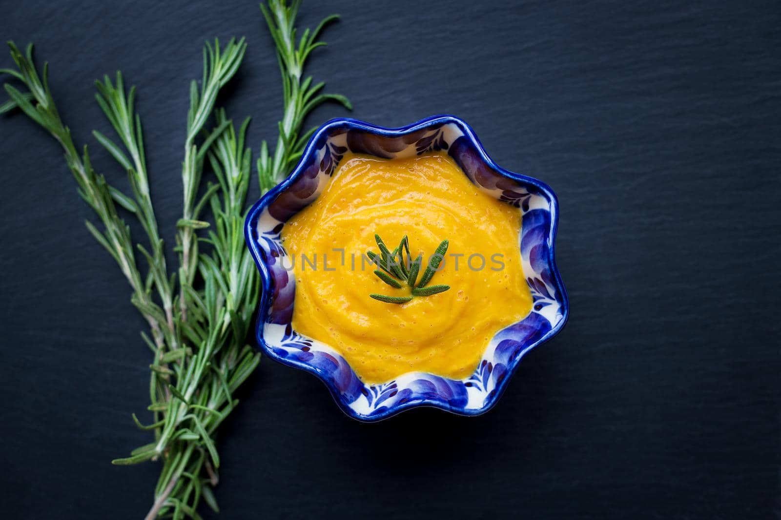 delicious pumpkin cream soup and black background with rosemary