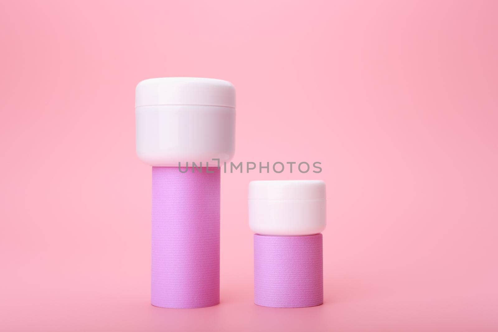 Set of two cosmetic jars with cream, lotion or balm on geometric shapes against bright pink background  by Senorina_Irina