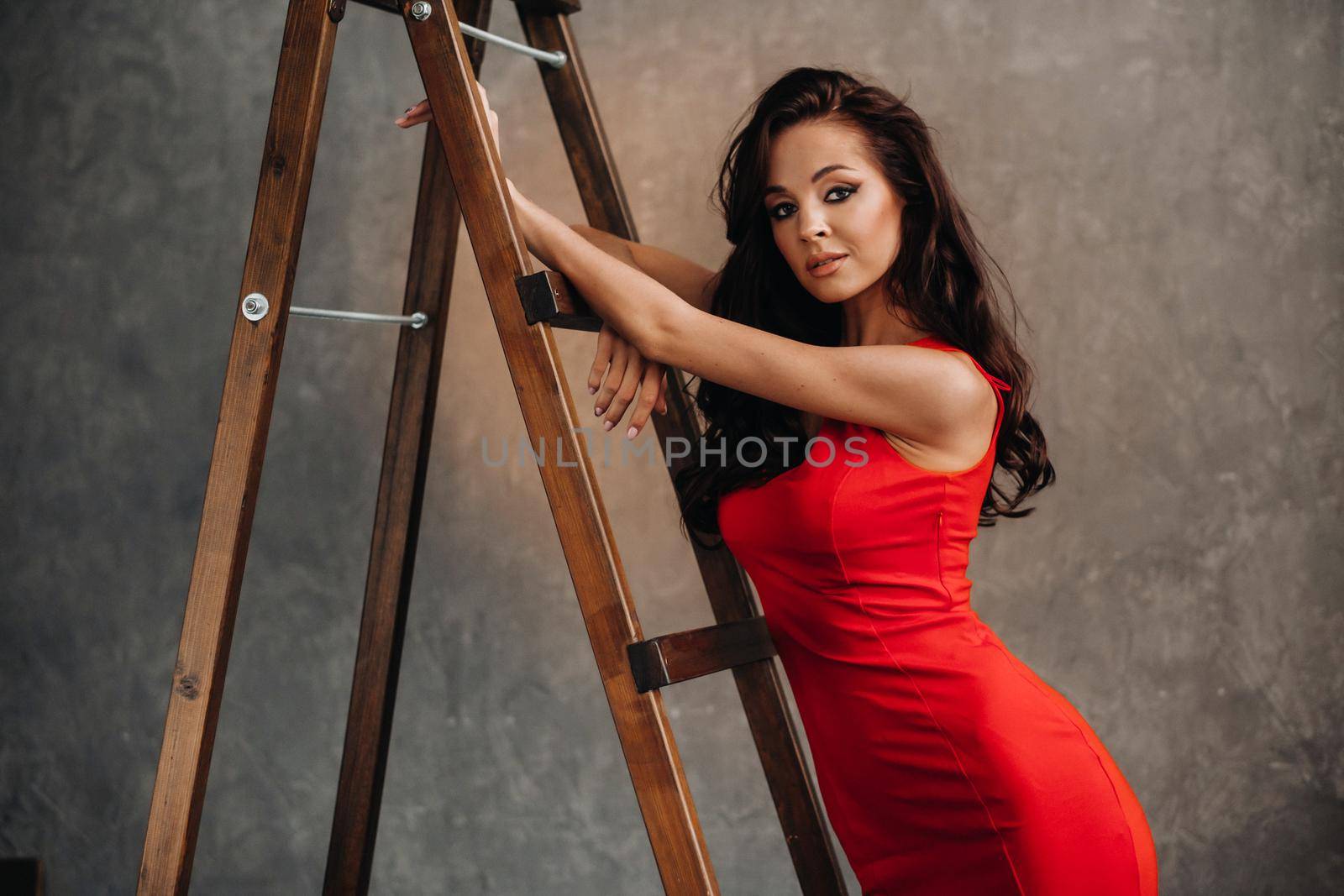 a brunette with long hair in a red dress poses in the studio near the stairs by Lobachad