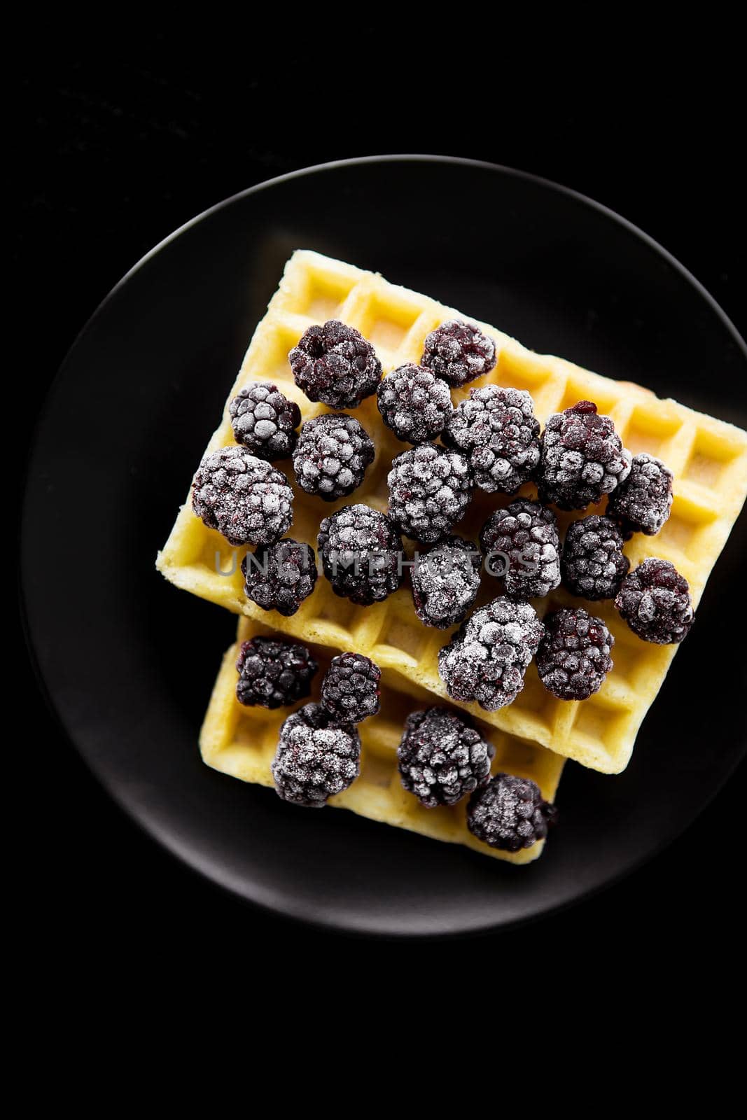 Belgian wafers with frozen blackberries on a black background, close-up.