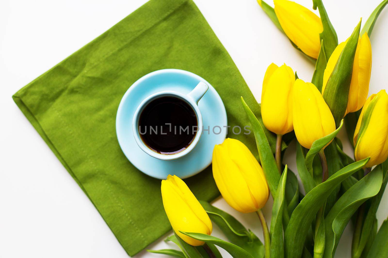 Yellow tulips with a cup of coffee on the white table with green cloth