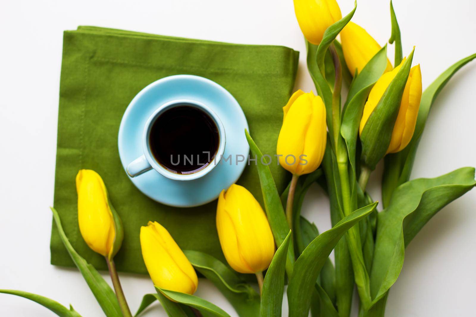 Yellow tulips with a cup of coffee on the white table with green cloth, close-up