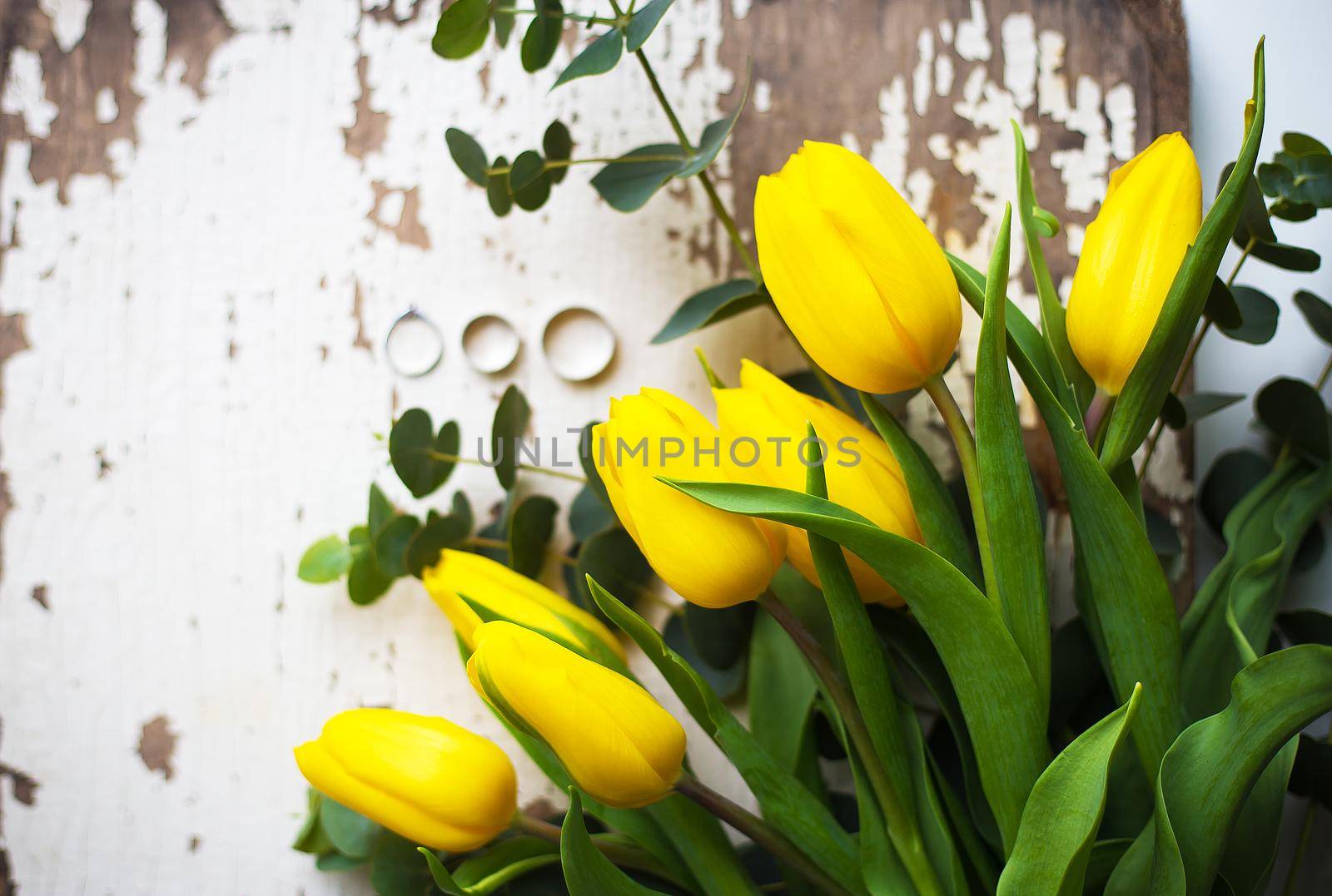 Beautiful wedding rings with yellow tulips on old white table