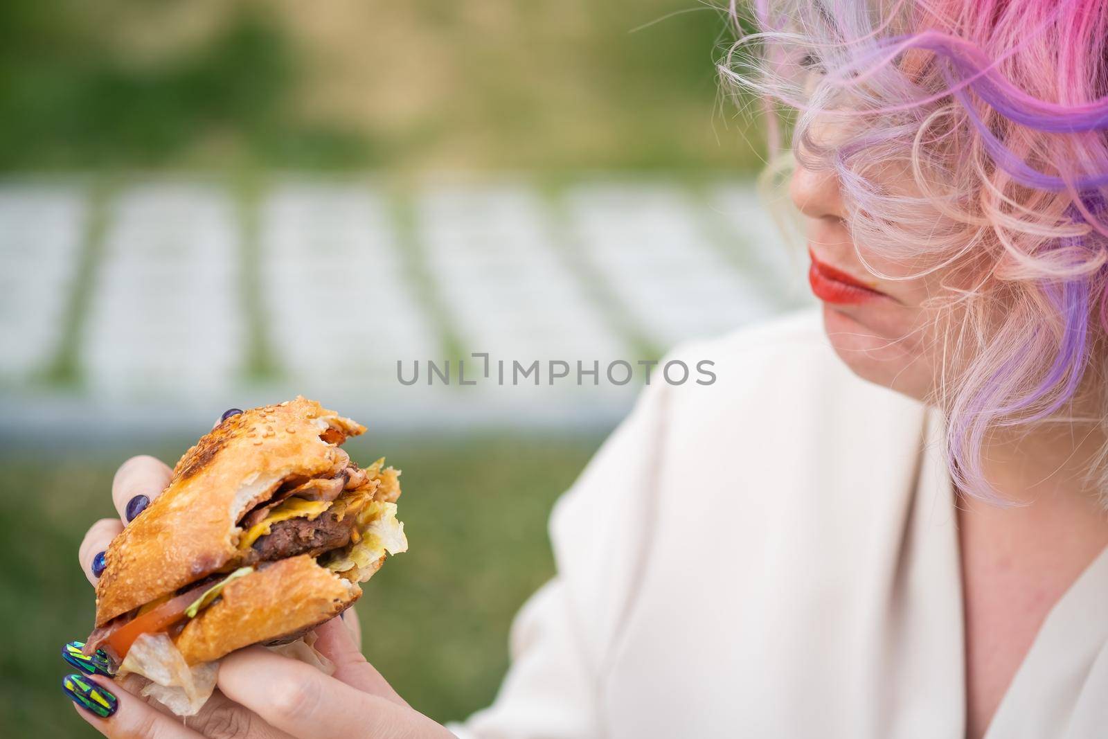 Caucasian woman with curly colored hair eating burger. Bad eating habits and love of fast food by mrwed54