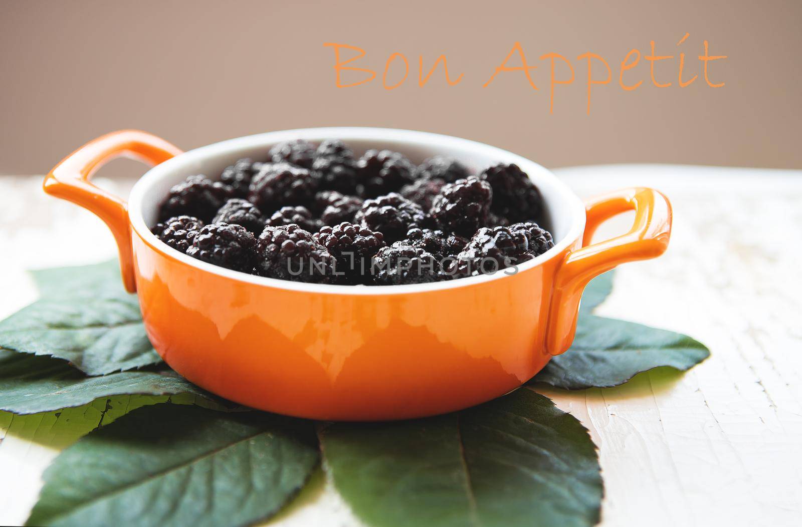 A full plate of blackberry stands on an old wooden background, the inscription bon appetit.