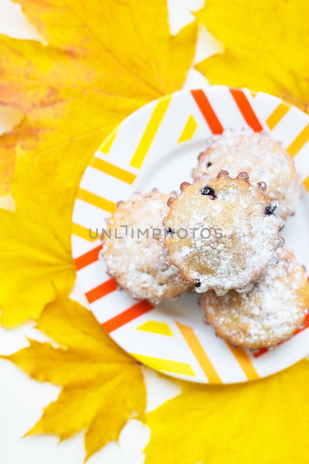 colored cupcakes on a plate and yellow autumn leaves, close-up