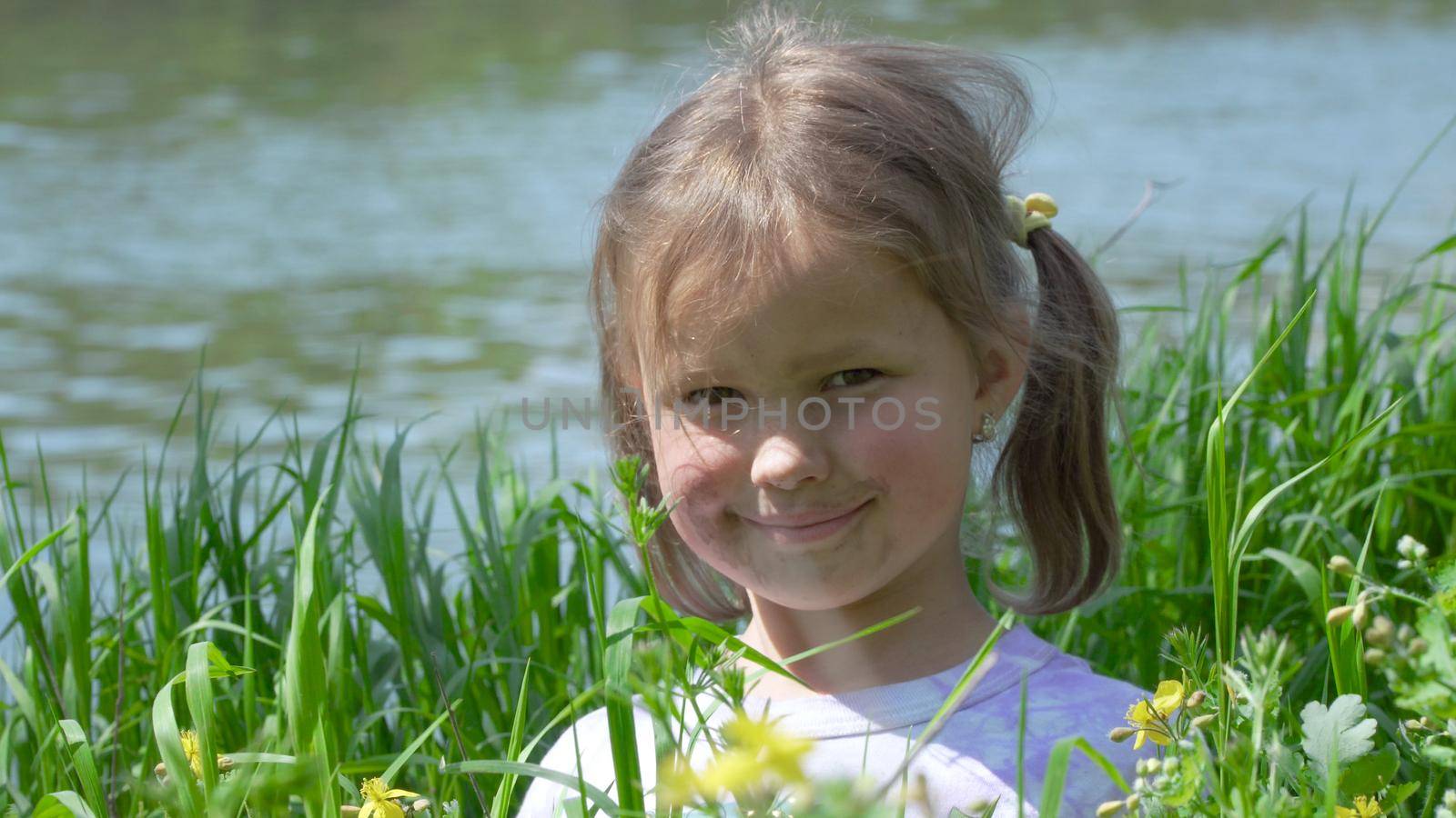 Portrait of a smiling little girl. Baby girl sitting in tall grass. Tiny kid have fun, enjoy nature outdoors.