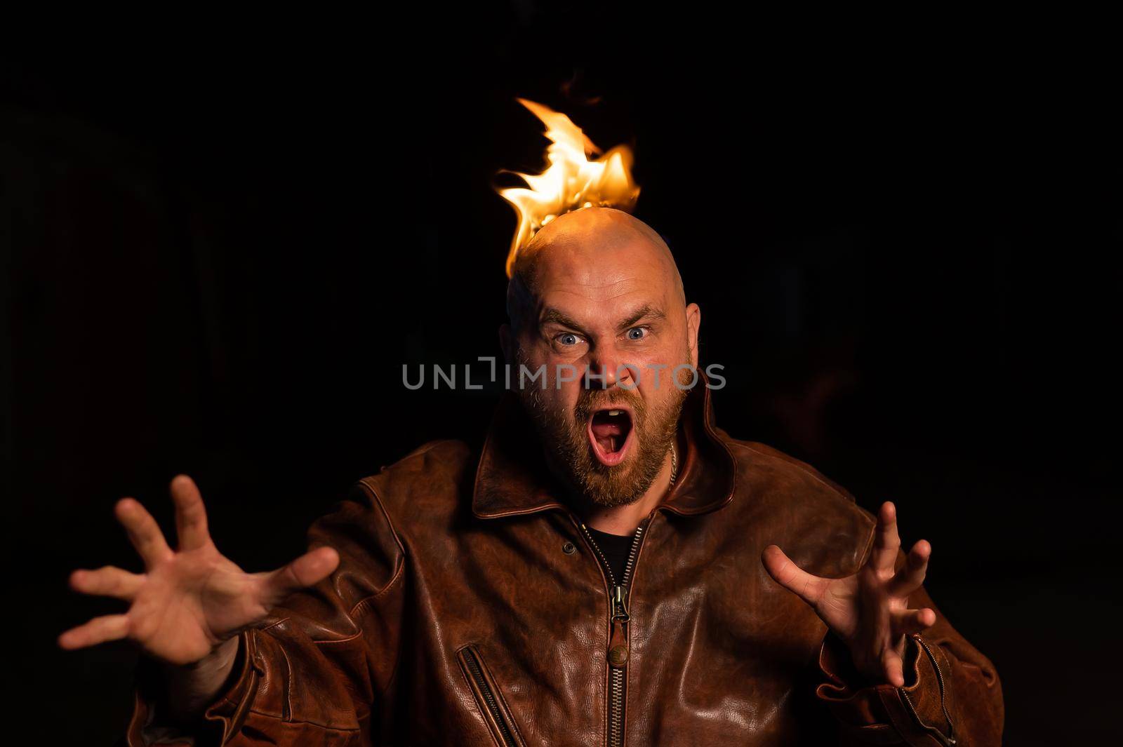 Bald man in a leather jacket with a burning head on a dark background