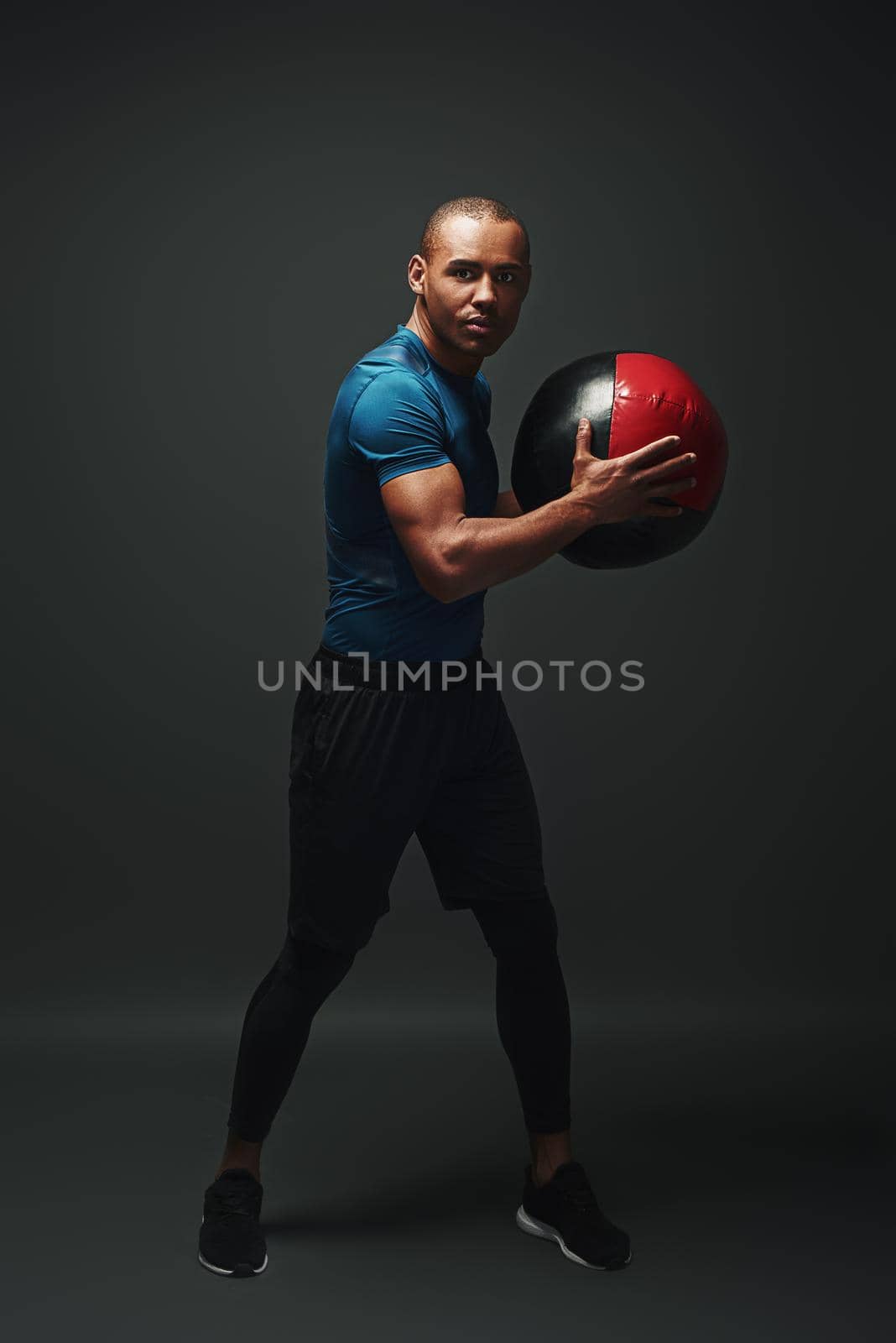 Full length shot of a crossfit male athlete working out with exercise ball. Handsome muscular athletic sportsman exercising with exercise ball over dark background in studio. Endurance concept