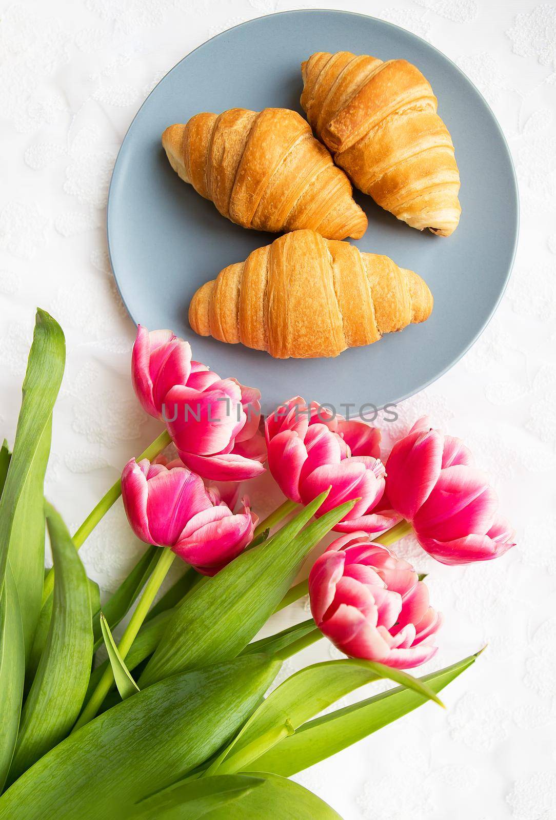 croissants on the background of laces on a white background with a bouquet of pink tulips.