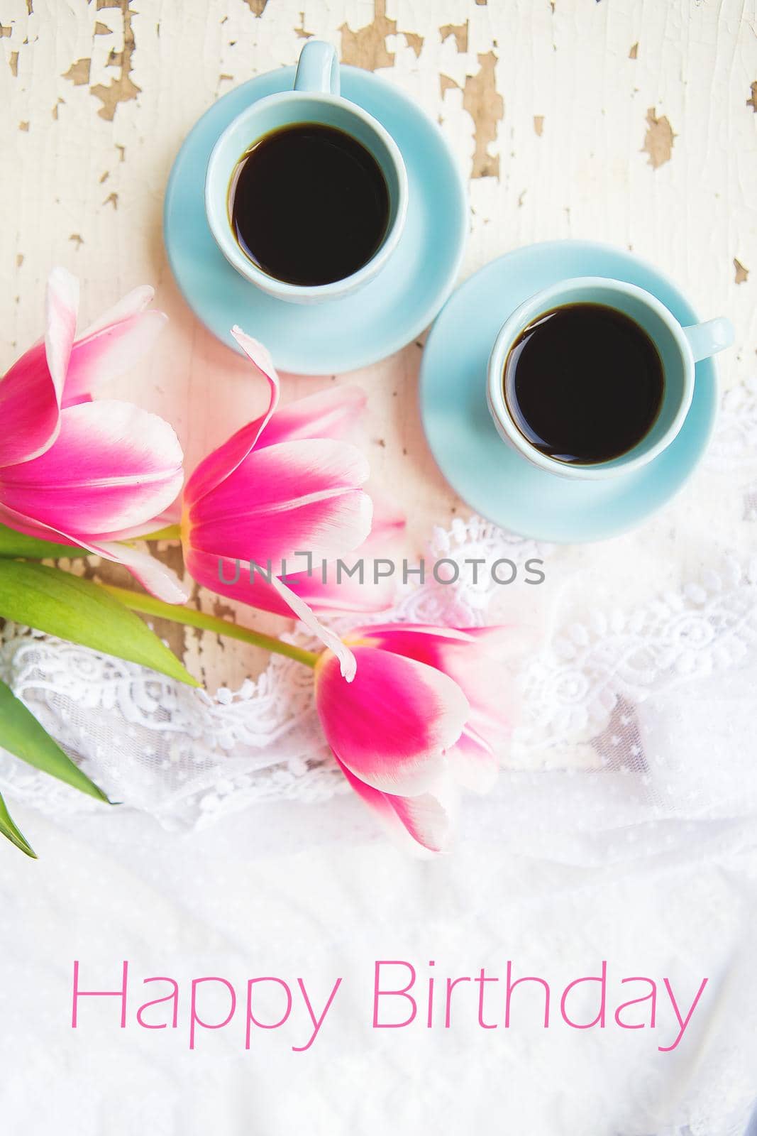 two cups of coffee and pink tulips on an old table, writing happy birthday by sfinks