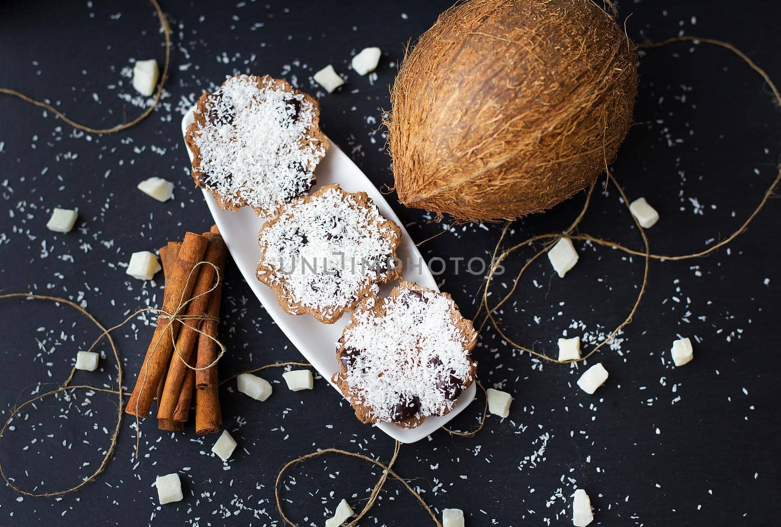coconut muffins on a black background with cinnamon sticks and whole coconut slices and candied