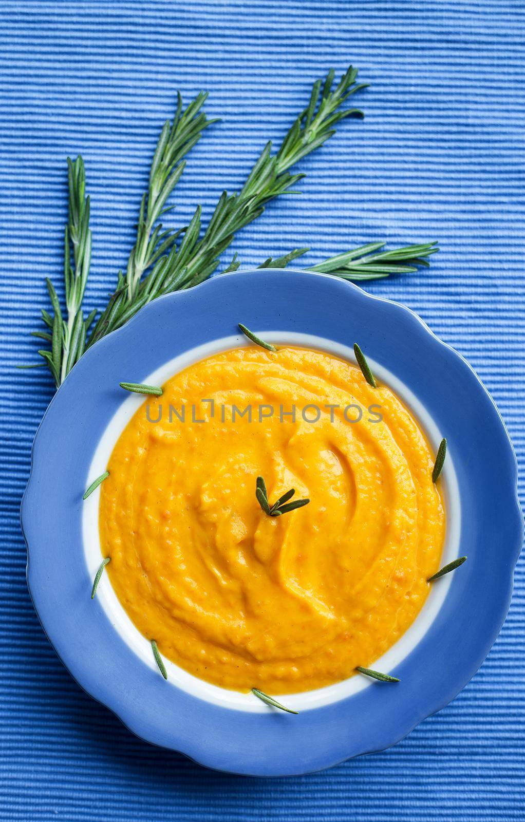 pumpkin cream soup in a blue plate on blue napkin, a branch of rosemary
