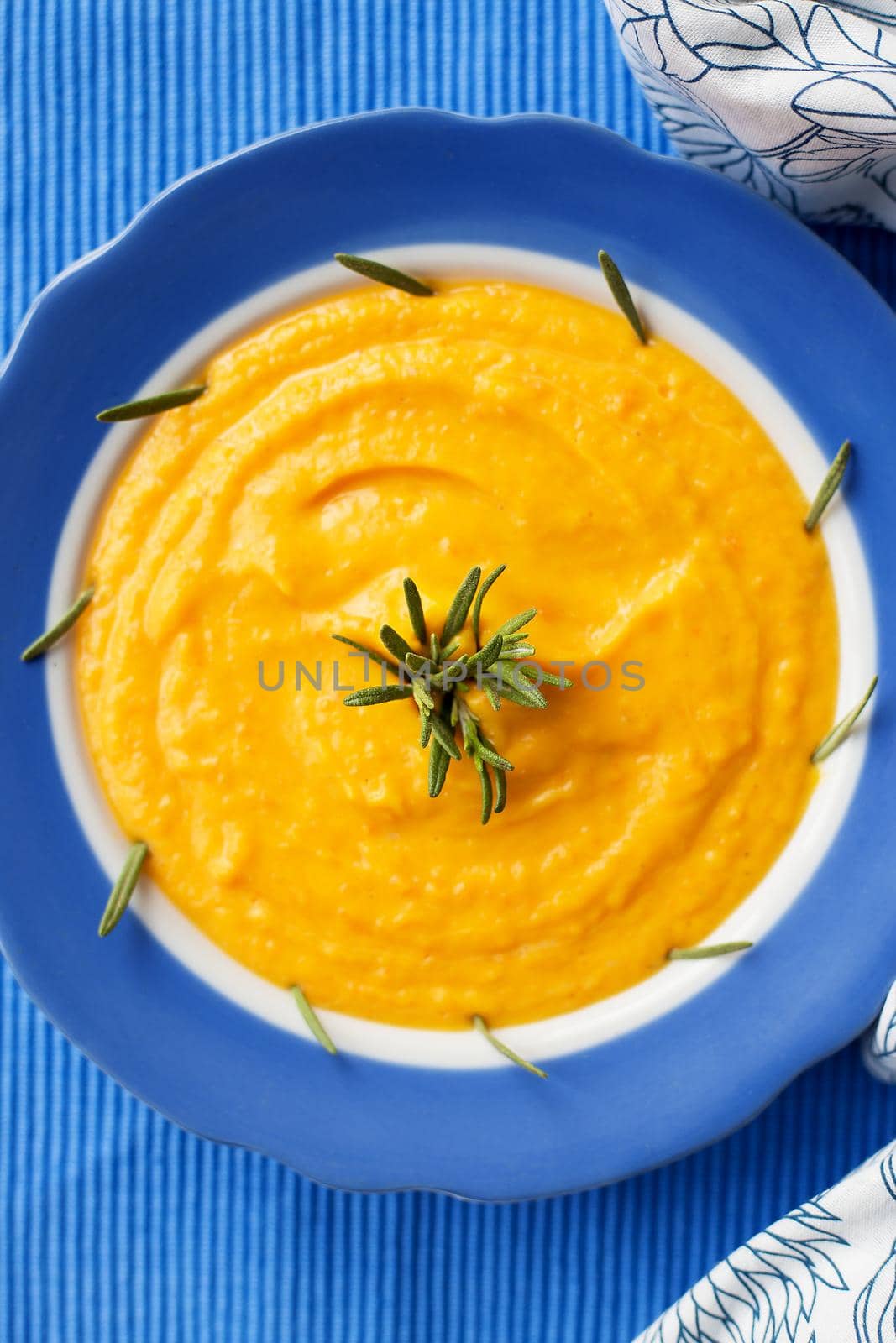 pumpkin cream soup in a blue plate on blue napkin with rosemary