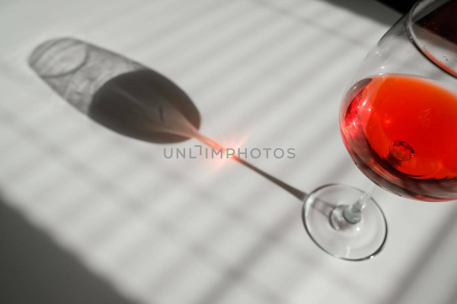 A glass of red wine on a white table with a shade from the blinds.