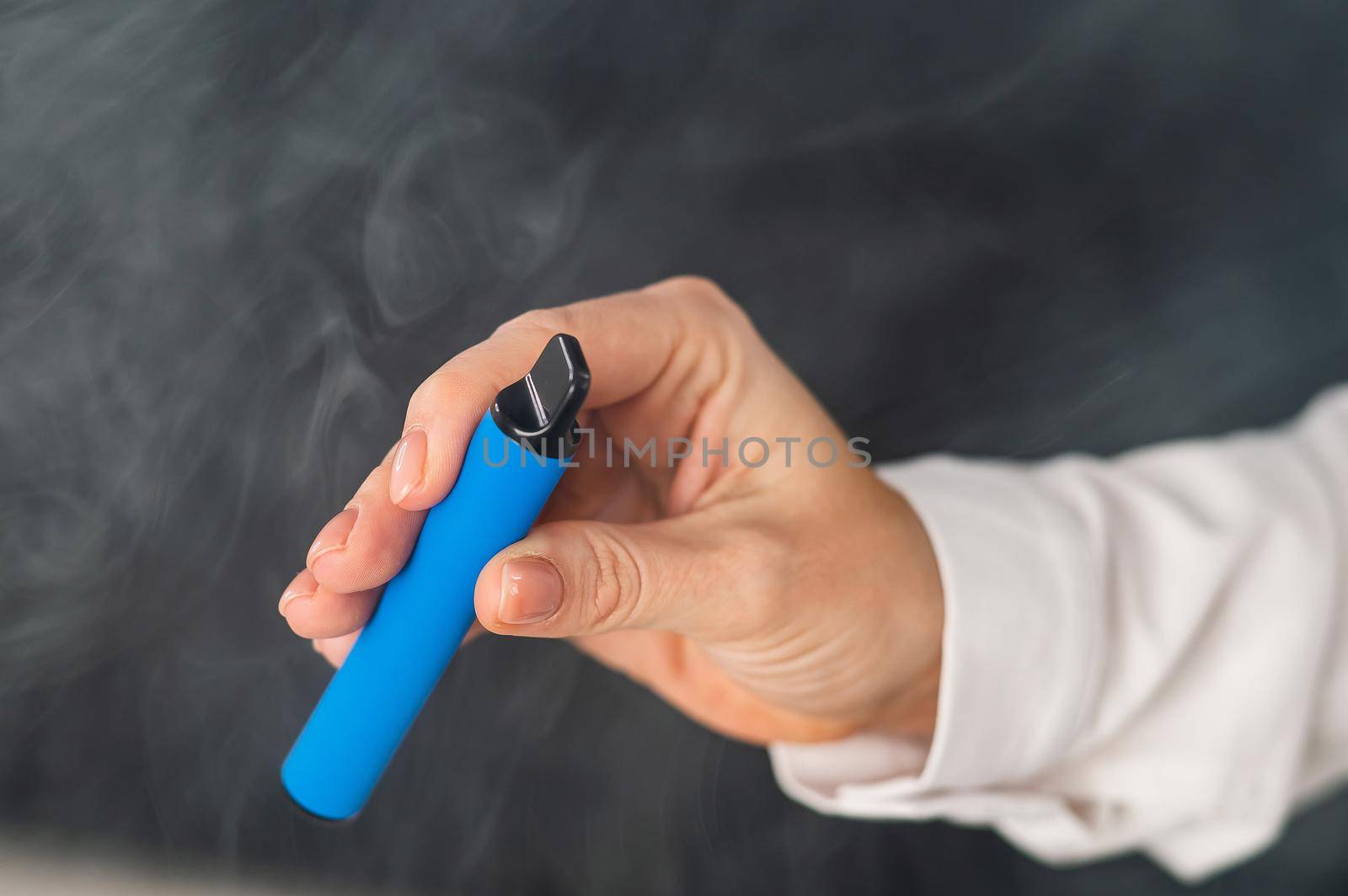 Caucasian woman smokes disposable vape on black background. Alternative device for smoking. Close-up of a female hand. by mrwed54