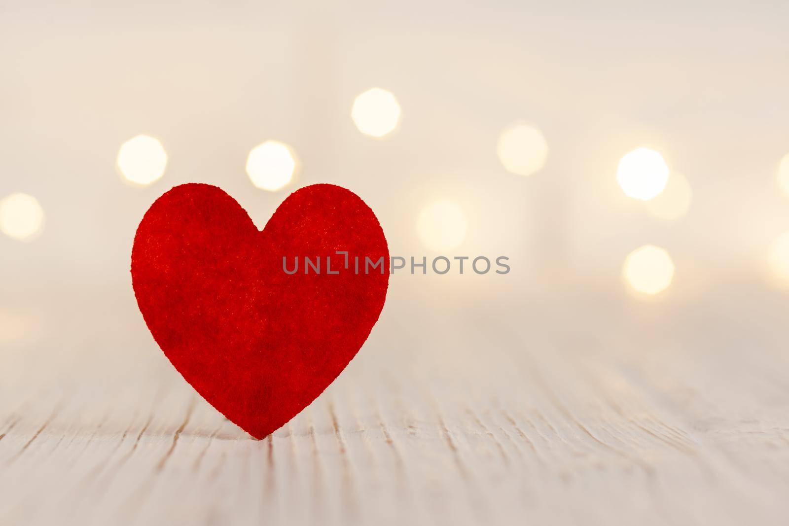 on a light wooden background a red heart, in the background the garland is out of focus