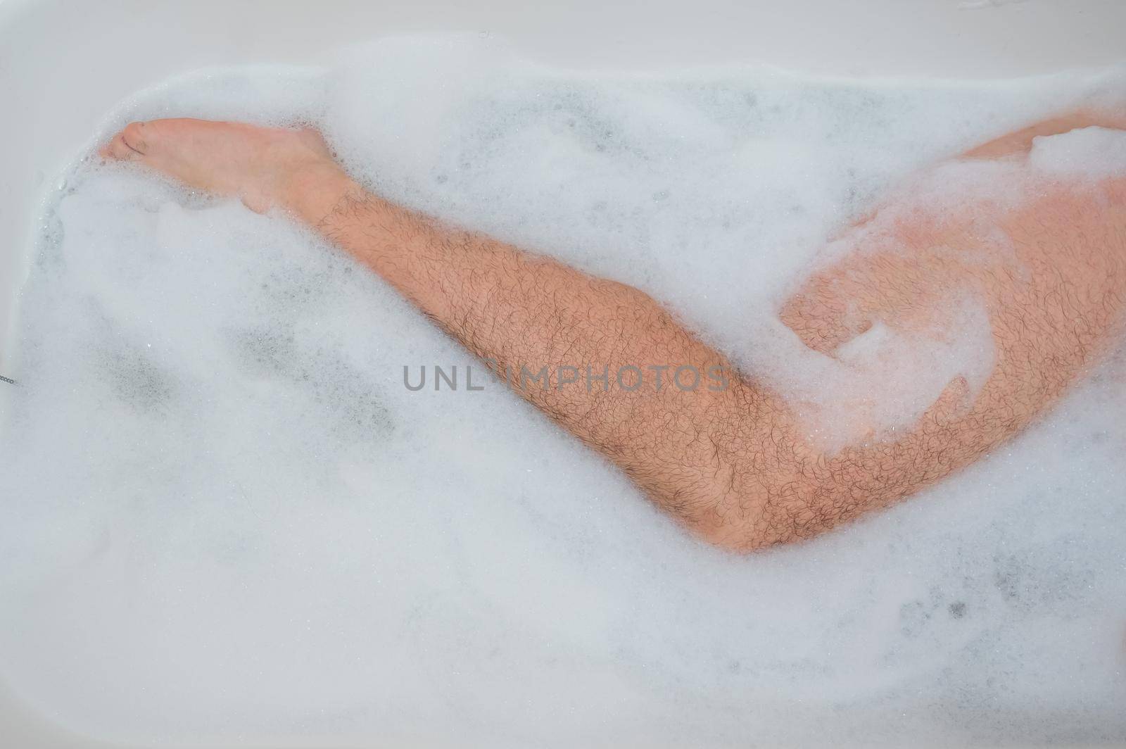 Funny picture of a man taking a relaxing bath. Close-up of male feet in a bubble bath. Top view by mrwed54