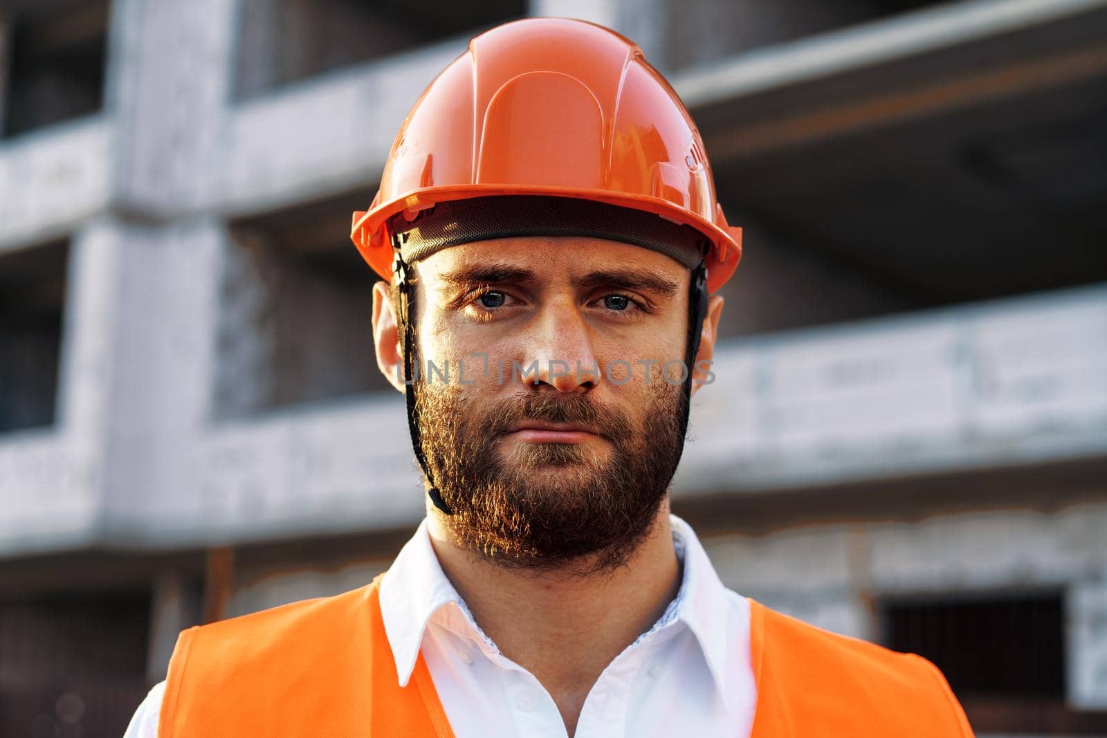 Builder wearing hardhat and safety vest standing on a commercial construction site, close up portrait