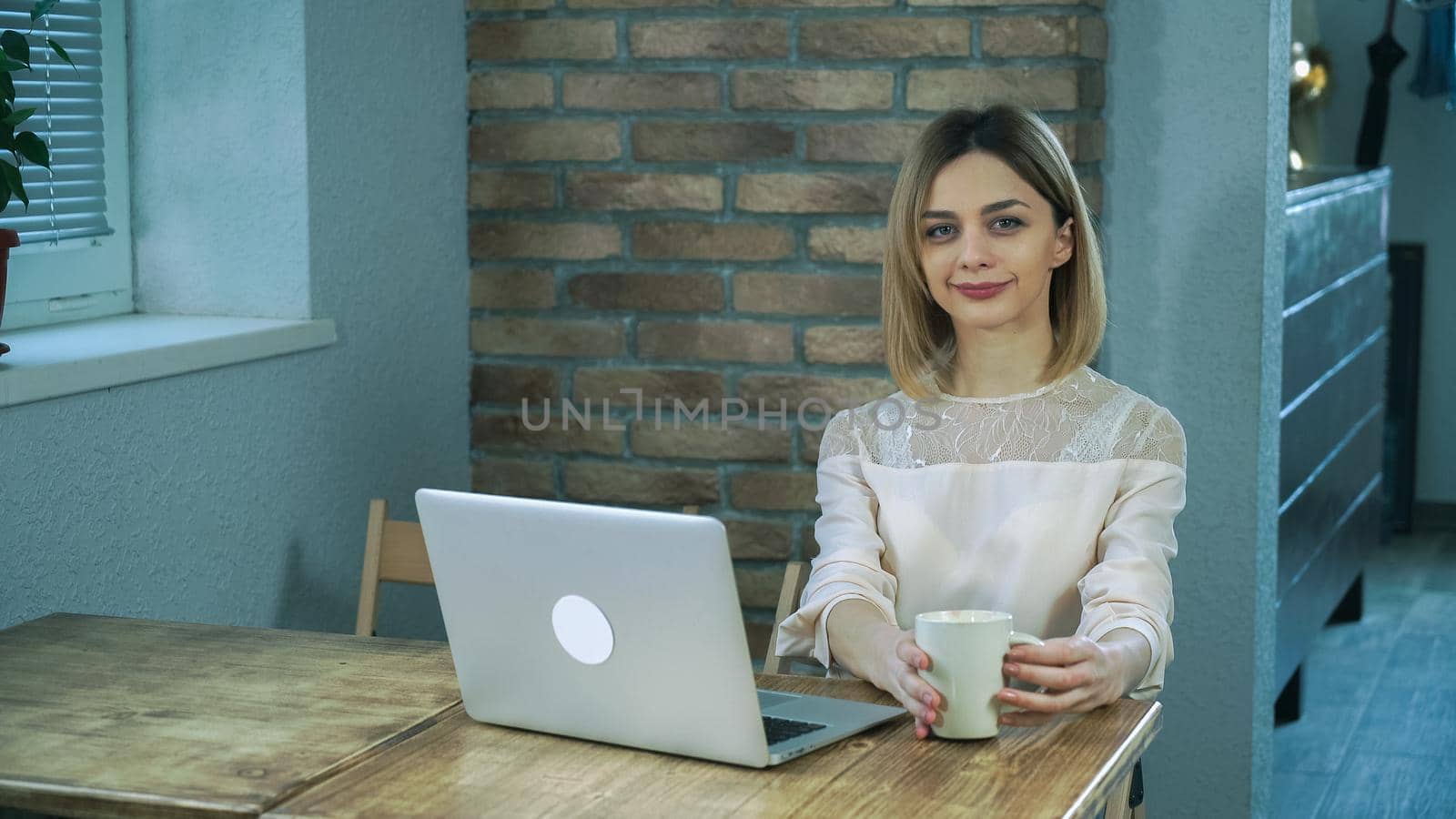 Young girl sitting in a cafe, at the computer, typing on the keyboard, drinking coffee, wearing a white blouse.