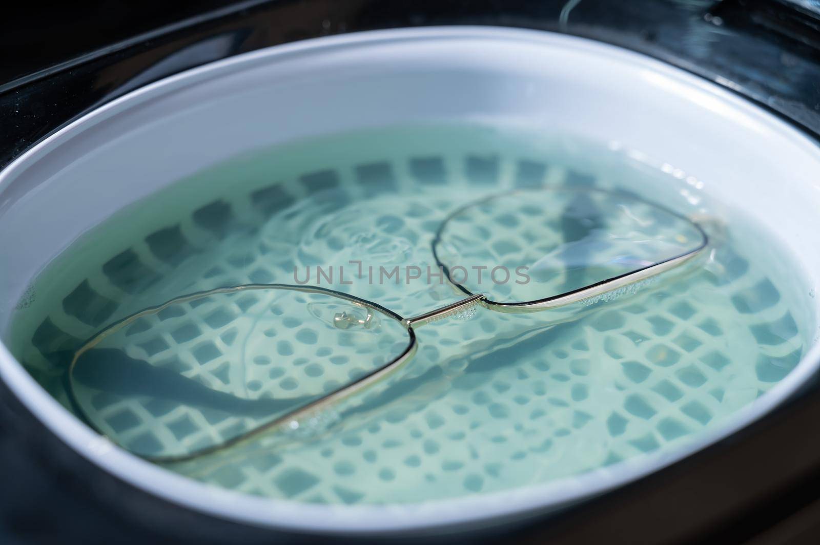 Ultrasound cleaning of glasses in solution. Optical technician repairs the frame of glasses.
